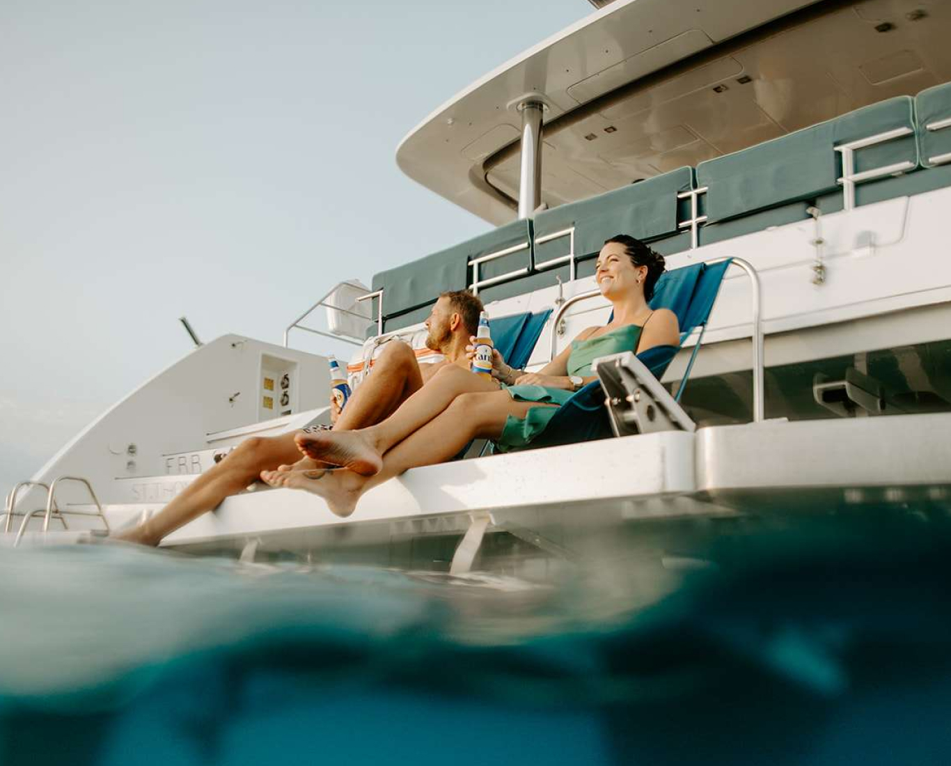 couple relaxing off the back of a yacht with feet skimming water