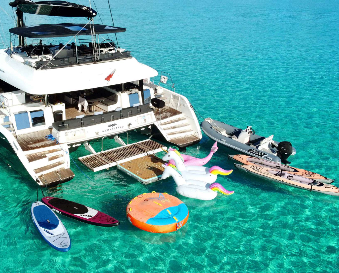 a yacht surrounded by floats, paddle boards, kayaks, and a dinghy